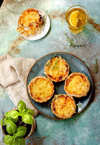 Mini quiches on a blue plate with glass of cold tea. Flaky dough pies. Fresh basil leaves and mini quiches on a blue background.