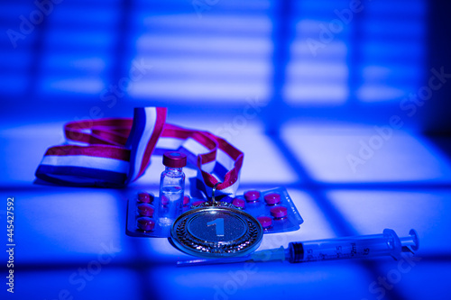 Champion gold medal, syringe with doping substance, pill tablet and vial with prohibited substance with lights and shadows of a curtain entering through the window at night. Sport and doping concept