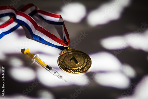 Champion's gold medal and syringe with doping substance with lights and shadows coming through the window. Sport and doping concept