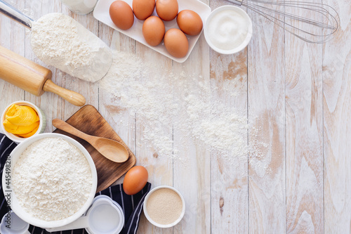 Homemade dough recipe (eggs, flour, milk, sugar) on a wooden table top view.