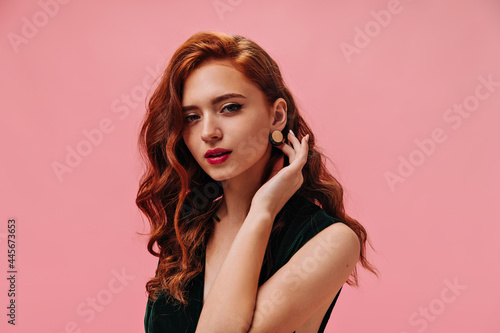 Red haired woman in green top looking into camera. Fashionable ginger girl with curly hair with red lips posing on isolated background..