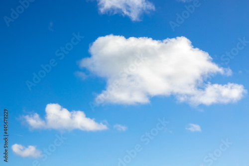 Close-up of three lined up white clouds against the blue sky, with the largest on top right and the smallest on left bottom