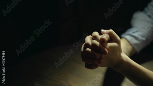 Close up of a woman’s folding hands on the table as she prays to God in a dark background