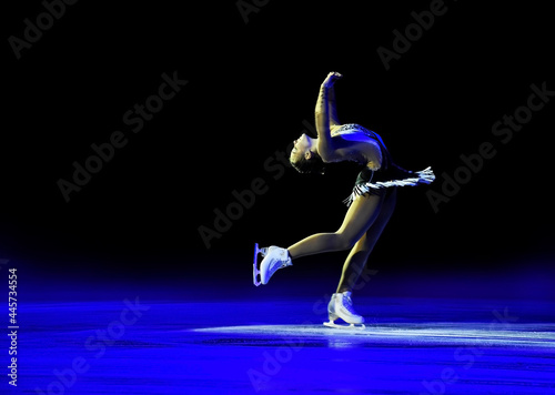 Reclined spin performed by a professional ice skater with artistic blue light and black background