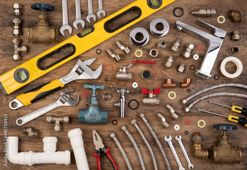 Plumber tools and spare parts on wooden background, top view, flat lay