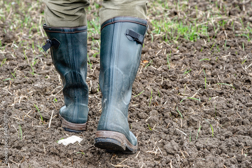 In autumn, a farmer goes with his green rubber boots over the freshly sown field.