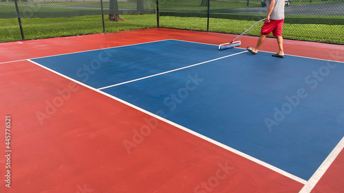 A pickleball court is dried using a squeegee