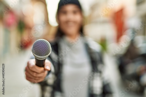 Young hispanic woman smiling happy using microphone at the city.