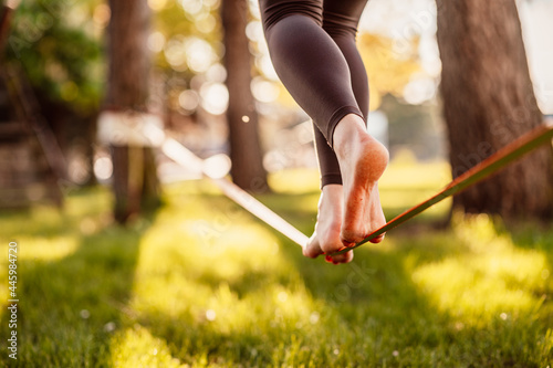 Slacklining is a practice in balance that typically uses nylon or polyester webbing. Girl walking on a slackline in a park during a sunset. Slack line