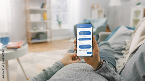 Man at Home Lying on a Couch and Using Smartphone for Chatting with His Girlfriend, Arranging a Date. Guy Using Mobile Phone, Talking Through Internet Social Network. Point of View Shot.