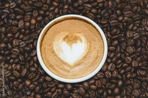 Zenith view of a cup of coffie with a drawn heart surrounded by coffe beans