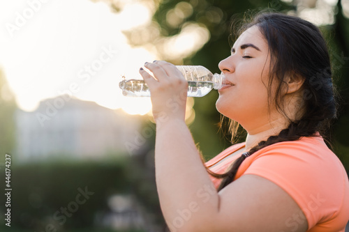 Dehydrated woman. Water thirst. Nutrition wellness. Body healthcare. Side view portrait of obese overweight drinking lady in defocused copy space sunset background.