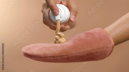 Dosing bronzing lotion or tanning cream from a flask with a doser to a pink tan applicator glove. High quality close-up studio photo image beige background.