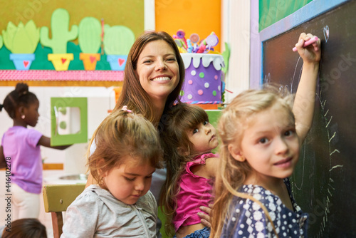 Kindergarten teacher and children while painting at the school blackboard