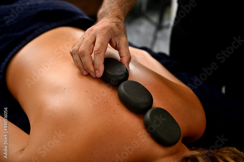 Close-up of masseur laying hot stones along spine of young woman. Ayurvedic hot stone massage in modern spa salon
