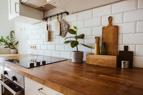 Kitchen brass utensils, chef accessories. Hanging kitchen with white tiles wall and wood tabletop.Green plant on kitchen background