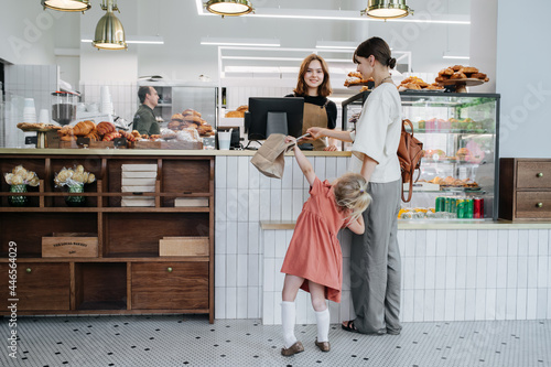 Woman paying for pastry in a bakery shop. Holding daughter by hand.
