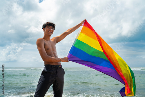 Portrait of young Hispanic gay boy looking at camera, holding LGBT flag - Focus on face landscape imagin