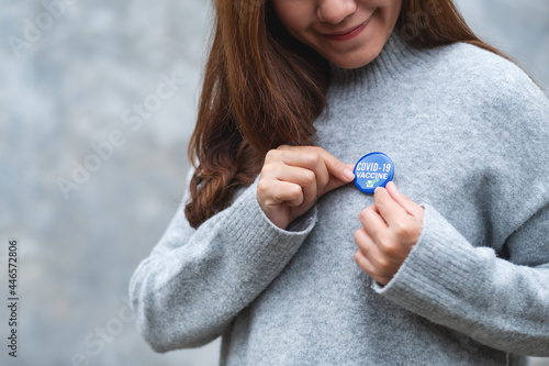 Closeup image of a young woman putting Covid-19 vaccinated sign brooch on shirt