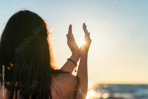 Silhouette of young woman's hands relaxing, happy meditating and holding sunset against golden hour sky on the beach.