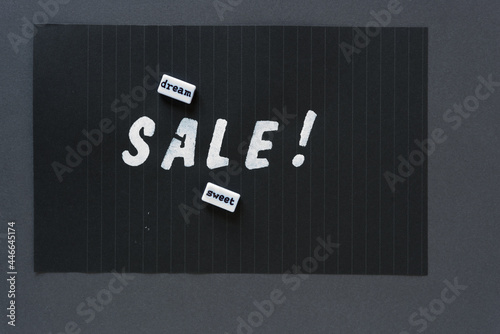 the word "sale!" in alpha/numeric plastic stencil letter type - hand painted in white acrylic paint - on black pad paper with faint lines and word beads "dream, sweet" - on dark gray paper