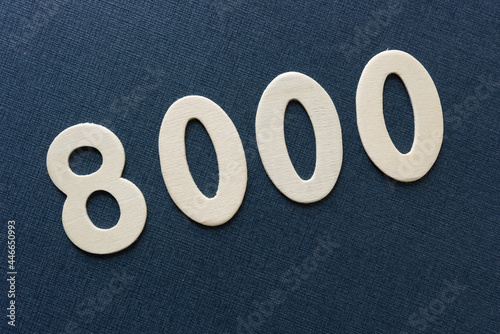 the number 8000 in plain untreated die cut wooden numbers on a dark blue background