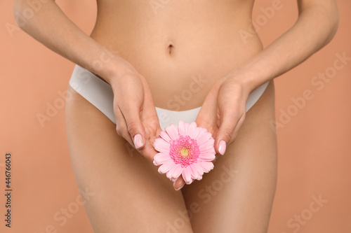 Woman in white panties with gerbera flower on peach background, closeup