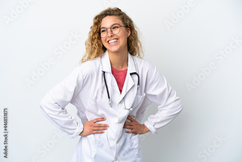 Young doctor blonde woman isolated on white background posing with arms at hip and smiling