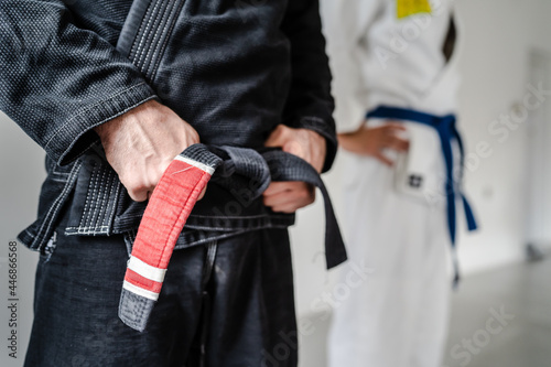 Side view of hand of unknown caucasian man in kimono gi standing while holding black bjj belt brazilian jiu jitsu concept copy space