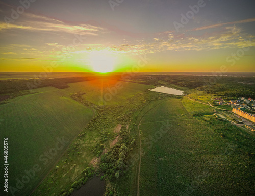 sunset over a green field and a lake. aero photo