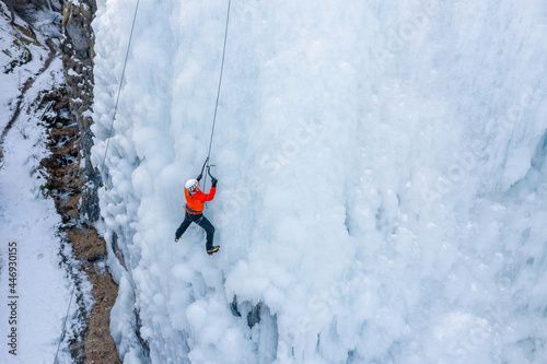 Male athlete climb cliff covered with ice, swinging the ice axe and using crampons to get a foothold