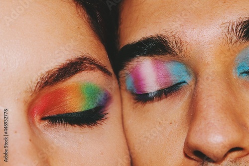 Closeup portrait of queer friends / young couple faces & eyes wearing eyeshadow makeup of lgbtq rainbow pride flag & trans pride flag