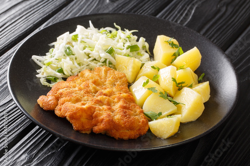 Fried pork cutlet breaded served with potatoes and cabbage salad close-up in a plate on a black wooden background. horizontal 