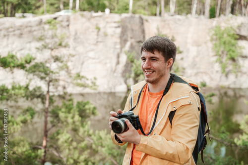 Joyful tourist man in a yellow raincoat takes pictures of trees near a stone quarry on a professional camera