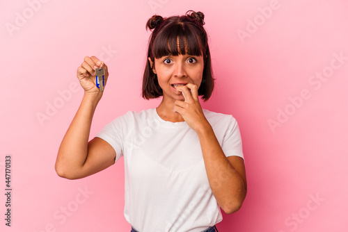 Young mixed race woman holding a keys isolated on pink background biting fingernails, nervous and very anxious.