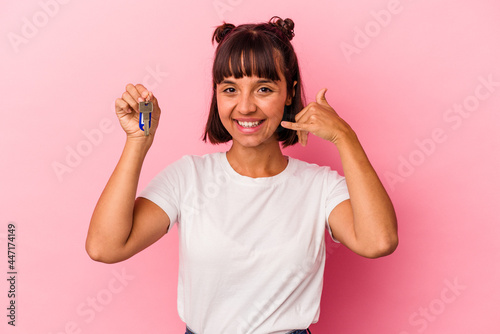 Young mixed race woman holding a keys isolated on pink background showing a mobile phone call gesture with fingers.