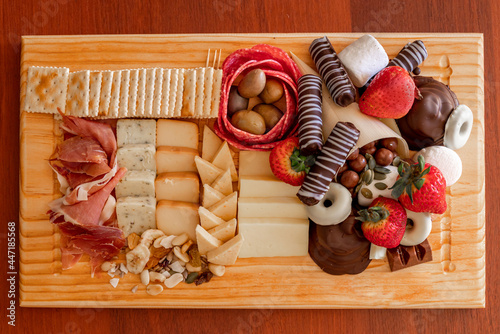 High angle view of a small cheese table with serrano ham, cookies, olives, nuts, strawberries and chocolate