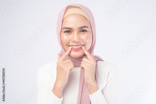 Young muslim woman holding colorful retainer for teeth over white background studio, dental healthcare and Orthodontic concept.