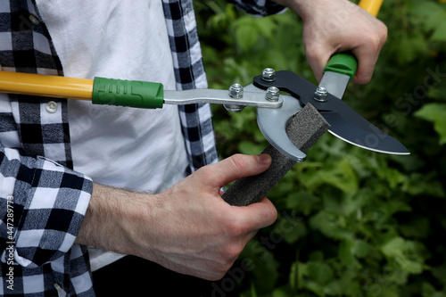 Man sharpening pruner outdoors, closeup. Gardening tools