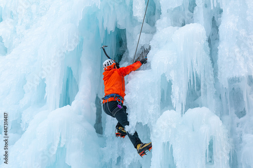 Athlete climbing cliff covered with ice, using ice axes, and piercing front crampons right onto the ice