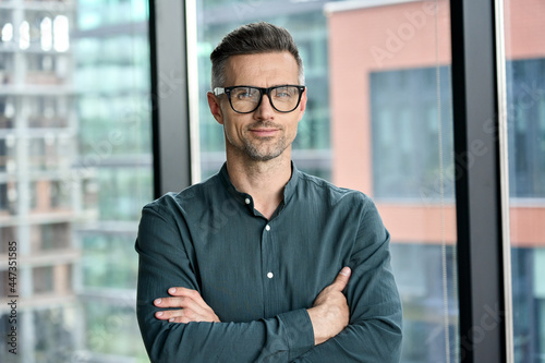 Smiling confident mature businessman looking at camera standing in office. Elegant stylish corporate leader successful ceo executive manager wearing glasses posing for headshot business portrait.