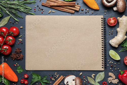 Open recipe book and different ingredients on black table, flat lay. Space for text