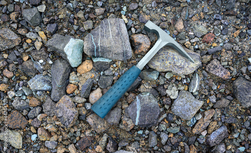 Steel geologists rock pick over background of multicolored serpentine rocks in asbestos mine