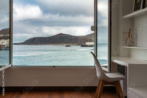 Atlantic ocean and landscape view through open window from inside home or hotel room with working table and chair. Work remote from home office in beach apartment. Gran Canaria, Canary Islands, Spain.