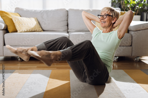 Happy senior woman doing sit-ups with hands behind her head in the living room