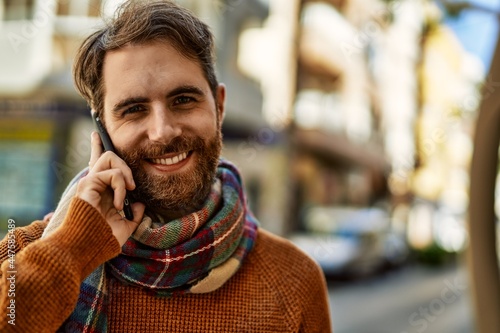 Caucasian man with beard having a conversation speaking on the phone outdoors on a sunny day