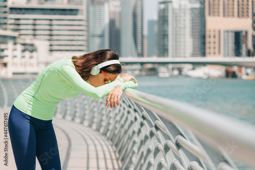 Woman suffering from shortness of breath or asthma leans against a fence and rests after a running workout on the embankment of Dubai Marina