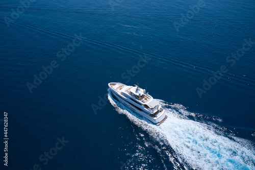 Superyacht is moving fast on the water top view. Motor Yacht in motion top view. A huge super Mega yacht in white on dark blue water in Italy. White yacht on the sea aerial view.
