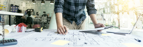 Interior designer or architect reviewing blueprints and holding pencil drawing on desk at home office.