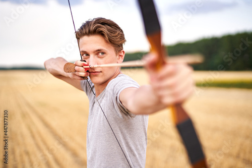 Young male sportsman targeting with traditional bow - Teenager archer practicing archery in nature - Outdoors sports and recreation concept with a millennial boy